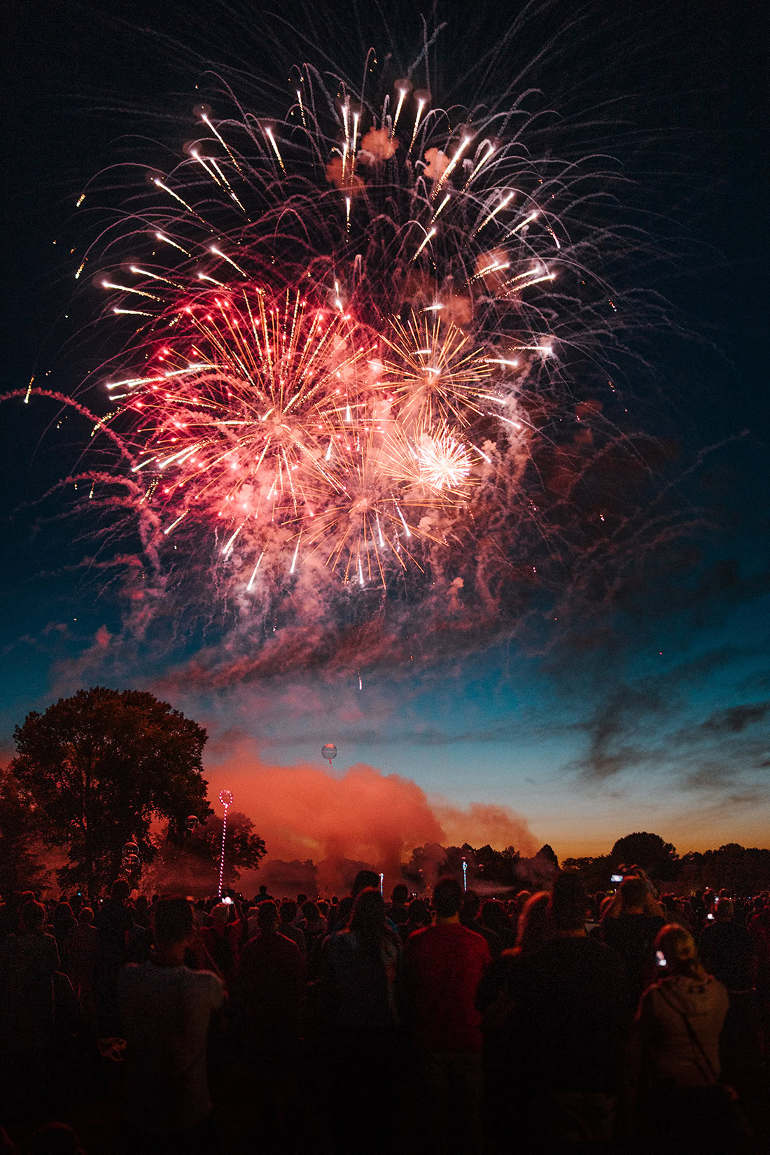 Menschen um mich herum blicken gemeinsam in den Himmel, während das Abschlussfeuerwerk der Kieler Woche in leuchtendem Rot und Gold über uns explodiert.