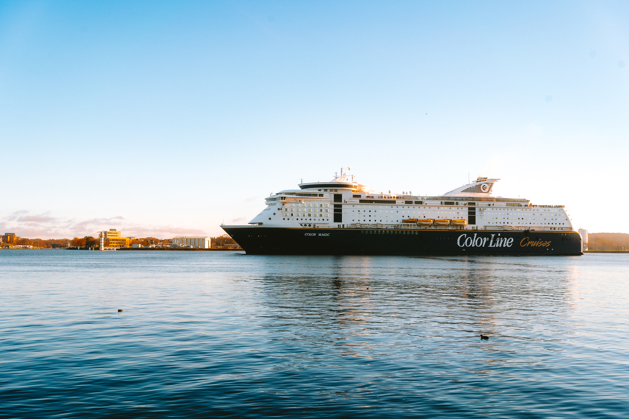 cruise ship glides through the calm waters of the Kiel Fjord, illuminated by the golden hues along the Kiellinie.